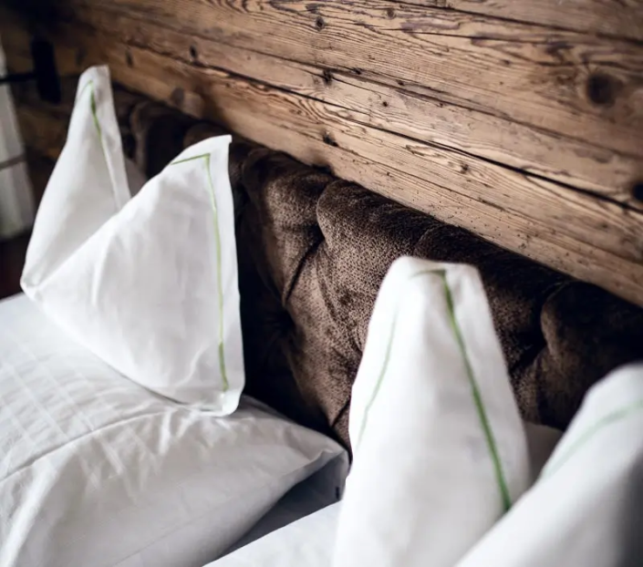 Hotel Gotthard Ein gemütliches Bett mit weichen weißen Kissen vor einer rustikalen Holzwand – alpiner Charme trifft auf modernen Komfort