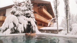 Entspannung pur im Winter – ein Gast genießt den beheizten Außenpool, während sanft der Schnee auf das Hotel Theodul und die verschneiten Tannen fällt