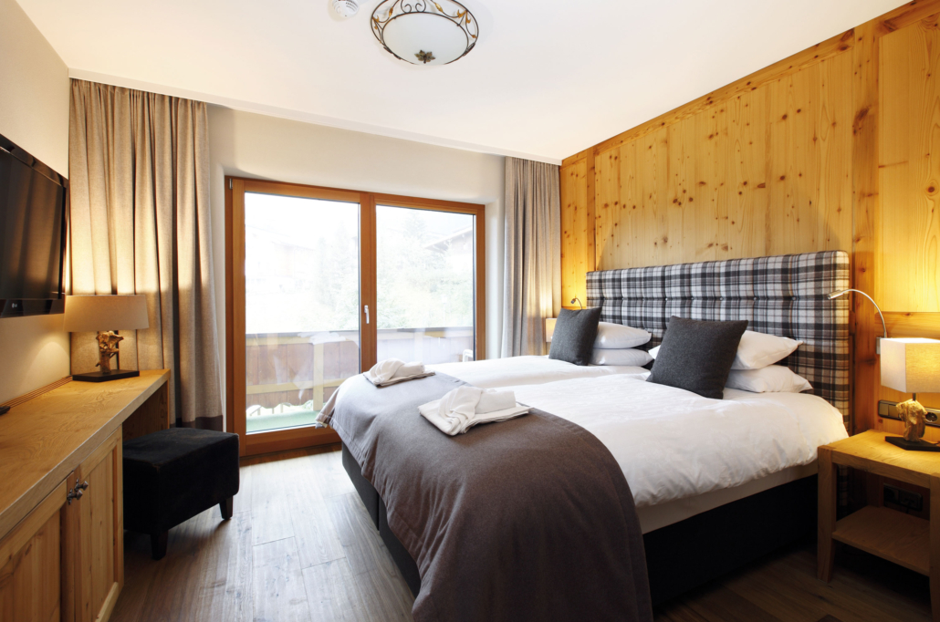 Gemütliches Doppelzimmer mit warmem Holz, stilvollen Stoffen und großem Balkon – ein Ort zum Ankommen und Wohlfühlen.