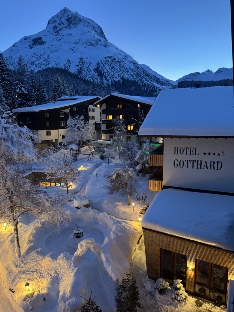 Verschneites Hotel Gotthard in Lech bei Abenddämmerung, umgeben von leuchtenden Wegen und winterlicher Berglandschaft